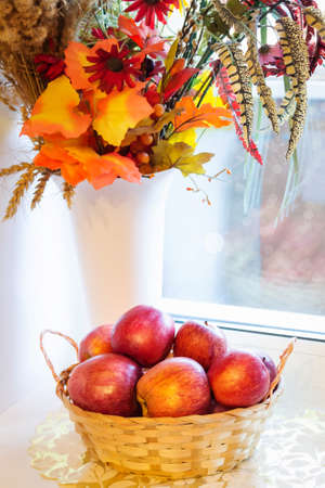Red apples in a wicker basket on a window on a sunny dayの写真素材
