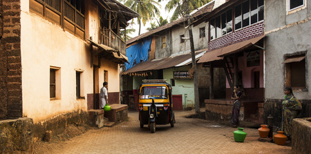 Gokarna, Karnataka, India- 29 January 2014 - yellow rickshaw and local people with jugs of water in a street.のeditorial素材