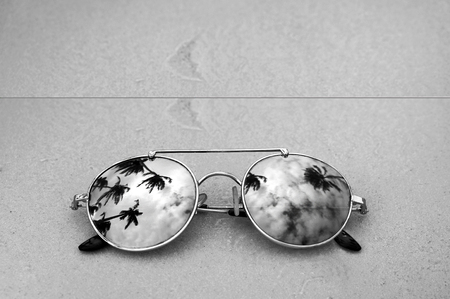 Mirrored sunglasses close up on the beach sand with palm trees reflection in black and white