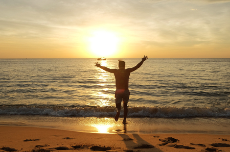 Happy man on the beach running to the sea at the sunsetの写真素材