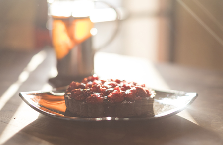 Raspberry tart with tea on wooden table in the sunlightの写真素材