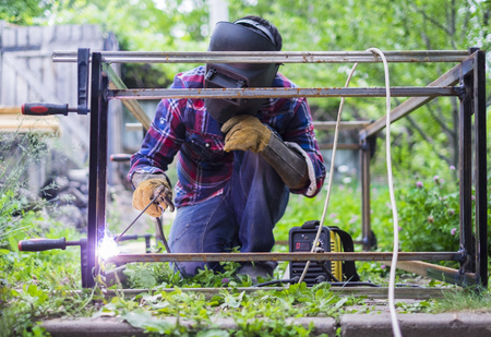 Man in a protective mask welding metal construction outside on a summer day