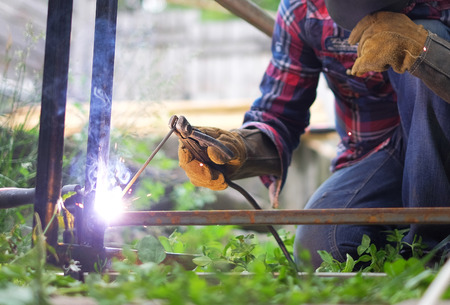 Man in a protective mask welding metal construction outside on a summer day