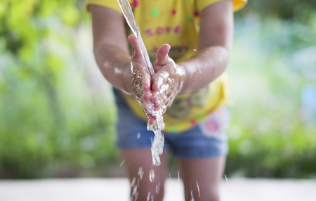 A girl washing hands outdoors on a summer day.の写真素材