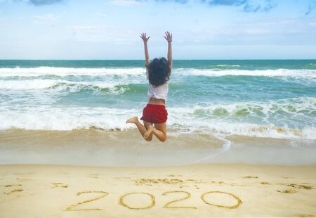 New Year 2020 on the sand, happy girl with hands up jumping on the beachの写真素材