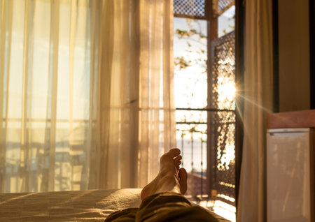 lying and relaxing in bed opposite a window at sunsetの写真素材