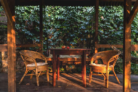 Cozy wooden gazebo with a round table and rattan chairs during sunsetの写真素材