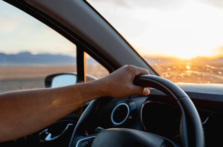 A man's hand on the steering wheel. Driving during sunset.の写真素材