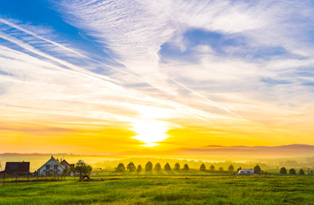 Early morning in the Czech village. Beautiful sunrise and colorful sky over a green field.の写真素材
