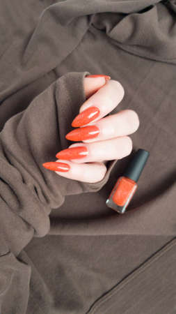 Female hand with long nails and orange ginger manicure holds a bottle of nail polishの写真素材
