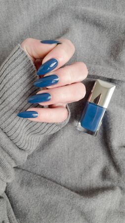 Female hand with long nails and blue manicure with bottles of nail polishの写真素材
