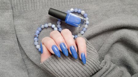 Female hand with long nails and blue manicure with bottles of nail polishの写真素材