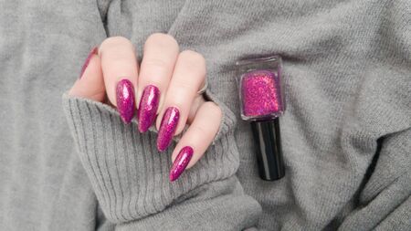 Female hand with long nails and pink fuchsia bottle manicure with nail polishの写真素材