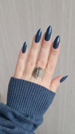 Female hand with long nails and blue manicure with bottles of nail polishの写真素材