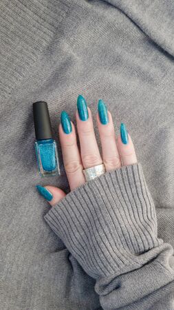 Female hand with long nails and turquoise blue manicure with bottles of nail polishの写真素材