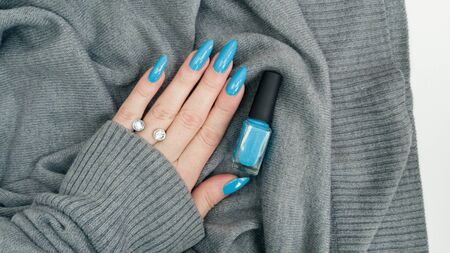 Female hand with long nails and turquoise blue manicure with bottles of nail polishの写真素材