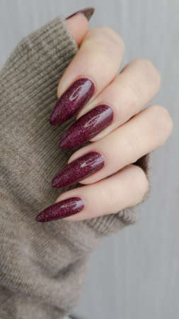 Female hand with long nails and a bottle of dark red nail polishの写真素材