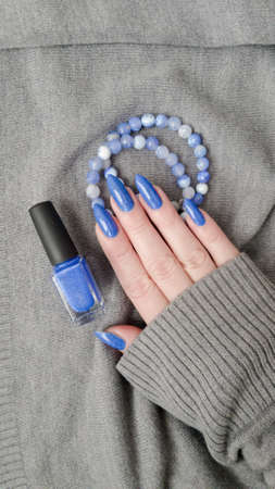 Woman beautiful hand with long nails and teal blue manicure with bottles of nail polishの写真素材