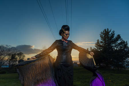 woman in a golden mask spikes on her face dancing with fans and shawls and posing at sunsetの写真素材