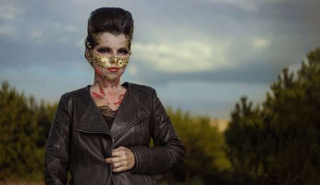 Actress woman in a golden mask spikes on her face dancing with fans and shawls and posing at sunset