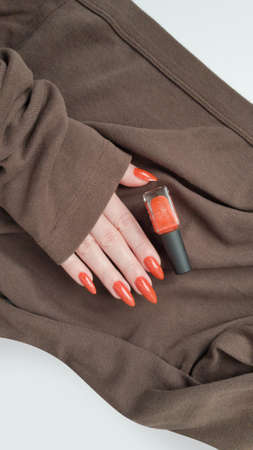 Female hand with long nails and orange ginger manicure holds a bottle of nail polishの写真素材