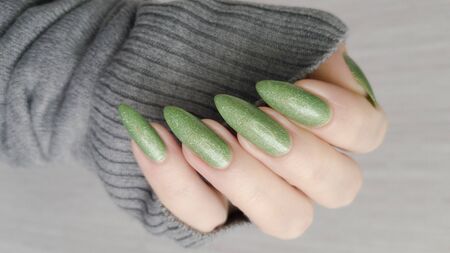 Female hand with long nails and a green manicure holds a bottle of nail polishの写真素材