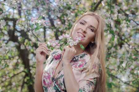 Blond girl with long hair in spring blooming apple orchard