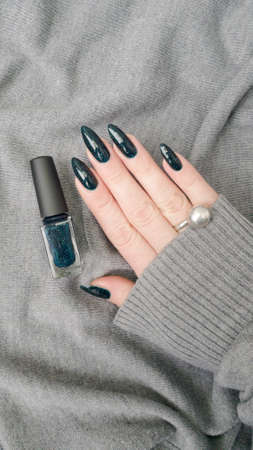 Female hand with long nails and blue manicure with bottles of nail polishの写真素材