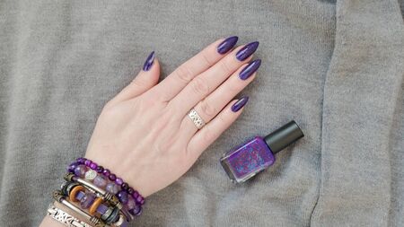 Female hand with long nails and a bottle of purple lilac color nail polishの写真素材