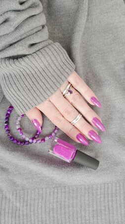 Female hand with long nails and a bottle of purple lilac color nail polishの写真素材