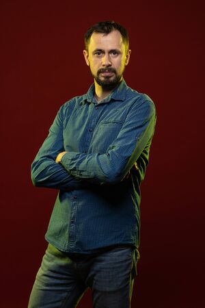 Brunette man with a beard posing on a red background in the studioの写真素材