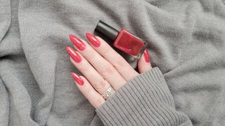 Female hand with long nails and a bottle of bright red nail polishの写真素材