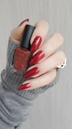 Female hand with long nails and a bottle of bright red nail polishの写真素材