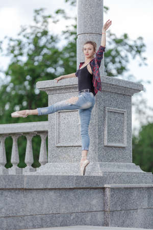 Girl ballerina in jeans, a plaid shirt and pointe shoes dancing in the city on the streetの写真素材