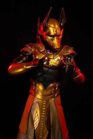 a male actor in a suit of an Egyptian mythology character, the golden deity Jackal Anubis, twists buugeng in red light on a black backgroundの写真素材