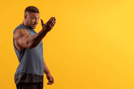 Emotional young male athlete bodybuilder in a gray T-shirt posing on a yellow background