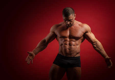 Young male athlete bodybuilder muscular torso posing on red backgroundの写真素材
