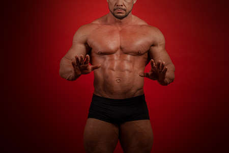 Young male athlete bodybuilder posing on a red backgroundの写真素材