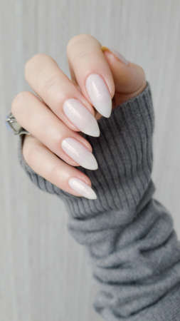 Female hand with long nails white manicure and a bottle of nail polishの写真素材