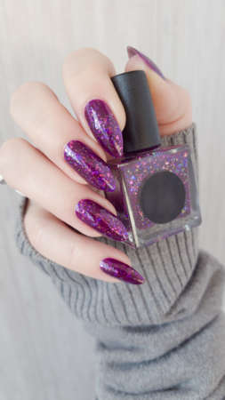 Female hand with long nails and purple lilac manicure holds a bottle of nail polish