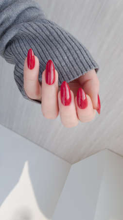 Woman hand with long nails and a bottle of dark red burgundy nail polish