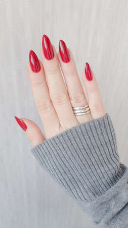 Female hand with long nails and a bottle of bright red nail polishの写真素材