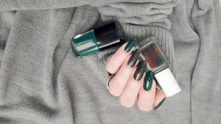 Woman's hand with long nails and green manicure with bottles of nail polishの写真素材