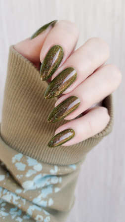 Woman's hand with long nails and green manicure with bottles of nail polish