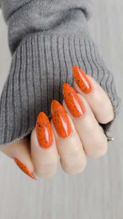 Woman hand with long nails and orange ginger manicure holds a bottle of nail polish