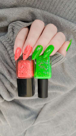 Woman hand with long nails and orange ginger manicure holds a bottle of nail polish