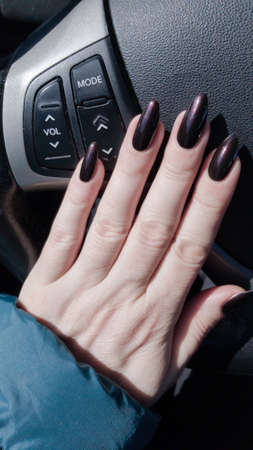 Female hand with long nails and black manicure with bottles of nail polishの写真素材