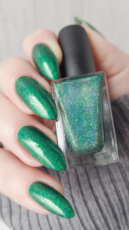 Woman's hand with long nails and green manicure with bottles of nail polish