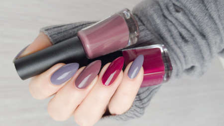 Female hand with long nails and multi-colored manicure, bottles of nail polishes