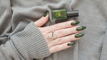 Woman's hand with long nails and green manicure with bottles of nail polishの写真素材